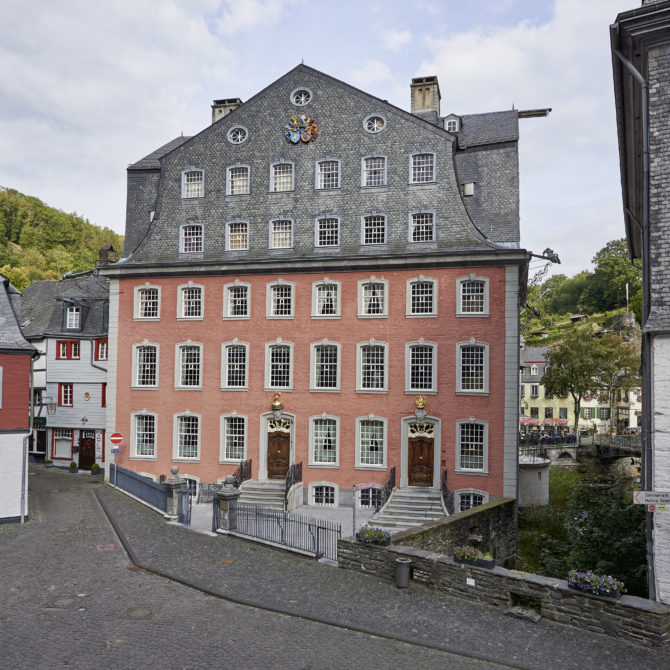 Fassade des Roten Hauses Monschau. Der Bau ist rosafarben getüncht, das Dach mit Schiefer gedeckt.
