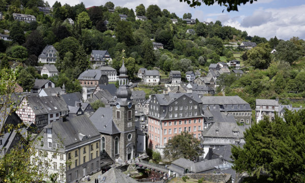 Blick hinunter auf die Häuser der Stadt Monschau. Zentral liegt das Rote Haus, daneben befindet sich eine Kirche.